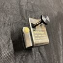 Kovový kapotastronom stříbrné barvy s černým plastovým šroubem. Na přední straně je žlutý štítek s nápisy fat)finger., USA Patent 4,840,102 a www.gro…