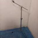 Stříbrný kovový mikrofonní stojan s boom ramenem a trojnožkou. Na konci ramene je umístěn zelený držák. Povrch stojanu vykazuje známky běžného opotře…