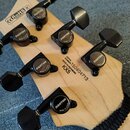 Záběr na hlavu kytary z přírodního světlého dřeva s šesti černými ladicími mechanismy. Na každém mechanismu je nápis GOTOH MADE IN JAPAN. Na zadní st…