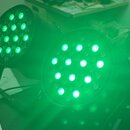 Dvě černé LED par lampy svítící zeleným světlem. Jsou umístěny na černém povrchu, v pozadí je vidět část transportního kufru. Na přístrojích nejsou ž…