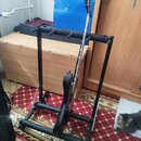 Černý kovový stojan na více nástrojů, v němž je umístěna černá elektrická kytara. Stojan má rámovou konstrukci s několika oporami pro krky nástrojů v…