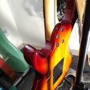 Zadní strana elektrické kytary s barevným přechodem od červené přes oranžovou k žluté. Tělo má v dolní části černý plastový kryt elektroniky a tři vi…