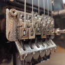 Detailní pohled na chromovaný kobylku typu tremolo s instalovanými strunami. Na kovové základní desce je vyryt nápis FloydRose Special. Povrch mechan…