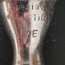 Detail stříbrného kovového moutky s vyraženými nápisy. Jsou zde vidět slova „Spezial“, „Runo Tilz“ a označení „S7E“. Povrch vykazuje drobné škrábance…