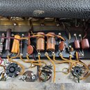 Fotografie zachycuje vnitřní elektroniku přístroje s komponenty rozmístěnými na černé desce. Jsou vidět různé typy kondenzátorů, rezistory a tři otoč…