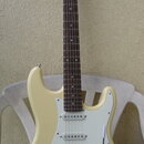 Elektrická kytara s krémovým korpusem a hnědým hmatníkem. Na hlavě je viditelný nápis Blond. Nástroj má tři snímače typu single-coil, bílý pickguard…