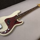 Elektrická basová kytara v krémové barvě s hnědým hmatníkem a červeně vzorovaným pickguardem. Na hlavě nástroje je viditelné logo Fender. Kytara má c…