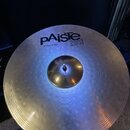 Fotografie znázorňuje kovový činel s koncentrickými rýhami na povrchu. Na horní části je černý nápis pAiste a vedle něj označení 20i BRONZE. Pod loge…