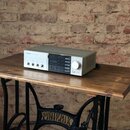 Stříbrný audio zesilovač s černým středovým panelem, umístěný na dřevěném stole. Na levé straně je nápis PIONEER a vedle něj text STEREO INTEGRATED A…