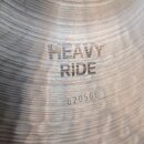 Detailní záběr na povrch kovového činele s viditelným rýhováním. Na povrchu je černý nápis HEAVY RIDE a níže vyražené sériové číslo 820566. Povrch vy…