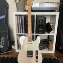 Elektrická kytara typu Telecaster v krémové barvě s bílým pickguardem a světle hnědým hnedem hmatníkem. Na hlavě je viditelné logo Squier. Nástroj st…