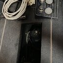 Fotografie zobrazuje černý reproduktor v otevřeném šasi a přilehlý ovládací panel s bílým napájecím kabelem. Na černém panelu jsou dva ovratové knofí…