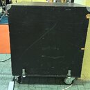 Černý, hranatý reproduktorový box z dřevěného materiálu. Povrch je viditelně opotřebovaný s mnoha škrábanci a odřesnými stopami, zejména v horní část…