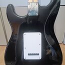 Zadní strana elektrické kytary s černým lesklým povrchem. Na kovovém spojovacím plechu u krku je nápis Squier. Uprostřed těla se nachází bílý plastov…