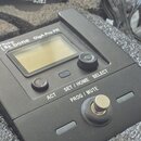 Černý elektronický přístroj s displejem, umístěný v polstrováním vystlaném pouzdře. Na horní hraně je nápis the ut.bone GigA Pro PR. Zařízení obsahuj…