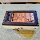 Fotografie zachycuje spodní stranu efekt pedálu v bílém provedení. Na černé spodní desce jsou nalepené informační štítky s nápisy BOSS AC ADAPTOR, Dr…