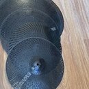 Čtyři černé kovové činely s perforovaným povrchem v různých velikostech. Na středovém vyvýšení nejmenšího činely je viditelný nápis ONE. Povrch nástr…