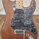 Elektrická kytara s hnědým dřevěným korpusem a světle hnědým hmatníkem. Nástroj má šedý mramorovaný pickguard a tři černé snímače s nápisem EMG. Na o…