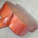Fotografie zachycuje zadní část krku a těla strunného nástroje z reddish-brown dřeva s viditnou masou. Povrch je lakovaný a vykazuje mírné oděry v mí…