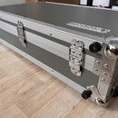 Šedý transportní kufr s hliníkovými hranami a kovovými rohy. Na horní části je bílý nápis ROCKBOARD® a pod ním menší text BY WAYWICK. Kufr má kovové…