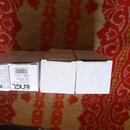 Tři bílé papírové krabičky umístěné vedle sebe na červeně vzorované podložce. Na levé krabičce je černý nápis „ENGL“, text „Handmade in Germany“, ozn…