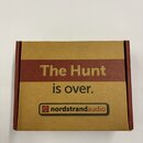 Hnědá kartonová krabice s červeným vodorovným pruhem. Na pruhu je nápis „The Hunt“, pod ním následuje text „is over.“. Ve spodní části je logo a náze…