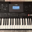 Černý digitální klavír s bílými a černými klávesami. Na horní části je nápis YAMAHA, displej s textem GrandPro a označení modelu PSR-E463. Nástroj ob…