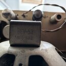 Detailní záběr na kovový, čtvercový komponent namontovaný na horní části reproduktoru. Na povrchu komponentu je vyražen nápis 8EV-52 a pod ním kód 46…