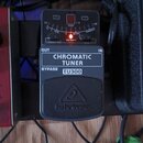 Černý chromatický tuner značky behringer, model TU300. Na horní části je displej s nápisy PITCH, BASS, GUITAR a CHROMATIC, doprovázný červený kontrol…