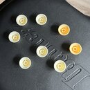 Osm bílých plastových krytek v podobě malých misiček s vnitřním křížovým žebrováním. Krytky jsou rozložené na černém povrchu z imitace kůže s vyražen…