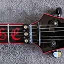 Detail hmatníku a hlavy elektrické kytary v černo-červené kombinaci. Na hmatníku je červeným Gothic písmem nápis RAGE a na hlavě bílé logo Schecter s…