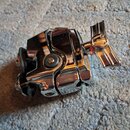 Fotografie znázorňuje kovový hudební příslušenství, pravděpodobně ladicí mechanismus, s chromovaným povrchem. Předmět má v pravé části plochou úchytn…
