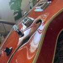 Detailní pohled na tělo polodubové elektrické kytary v oranžovém lesklém provedení s krémovým lemováním. Na povrchu jsou vidět dva chromované snímače…