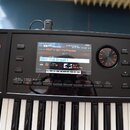 Černý digitální klavír s bílými a černými klávesami. V horní části je displej, na kterém jsou viditelné nápisy STUDIO SET PLAY, 001-Pythagoras, PRST…