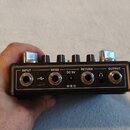 Fotografie zachycuje zadní panel černého kytarového efektu s kovovými potenciometry. Na panelu jsou čtyři konektory jack a jeden USB port s dopisemi…
