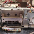 Fotografie zachycuje vnitřní mechanismus a elektroniku rozdaného kazetového přehrávače bez vnějšího krytu. V centru je vidět kovový mechanismus pro v…