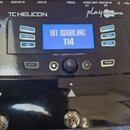 Černý efektový pedál s nápisy TC HELICON a play ACOUSTIC. Modrý displej zobrazuje text HIT DOUBLING 114 a pod ním VOCAL + HARMONY FX + GUITAR FX. Na…