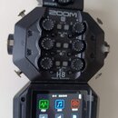 Černý digitální záznamový systém ZOOM H8 Handy Recorder. Zařízení má v horní části čtyři ovratové ovládací knoflíky s popisky MIC IN 1, 2, 3 a 4 a ná…