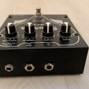Černý kytarový efekt s čtyřmi ovládacími knoflíky a stomečem. Na horní straně jsou popisy VOLUME, TREBLE, BASS a GAIN, v zadní části nápisy DC 12V, O…