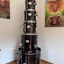 Sada bubnů v tmavě vínové barvě s chromovaným kováním. Na každém z pěti viditelných kotlů je umístěn oválný štítek s nápisem Pearl. Povrch nástrojů j…