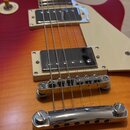 Detail elektrické kytary s červeno-oranžovým přechodem barvy (sunburst). Nástroj má dva snímače typu humbucker s kovovými kryty, krémový pickguard a…