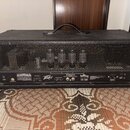 Zadní strana černého kytarového komba s texturovaným povrchem a kovovou mřížkou, skrze kterou jsou vidět elektronické součástky. Na spodním panelu je…