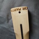 Fotografie zachycuje dřevěný krk nástroje světlé barvy s tmavým hmatníkem. Na horní hraně je vypálený nápis DR.PARTS. V dřevě se nachází jeden vyvrta…