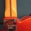 Detail zadní strany krku a těla elektrické kytary v červené barvě. Na kovém krytu spojení krku s tělem je vyryto logo Fender a nápis CORONA CALIFORNI…