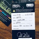 Fotografie zobrazuje papírový štítek s technickými údaji a doprovodné dokumenty značky PRS GUITARS. Na štítku jsou ručně vyplněné údaje: STRINGS 10-4…
