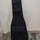 Černý poloměký pouzdro (gig bag) na kytaru. Má dvě zipované kapsy s okrajem v hnědé barvě, jednu menší v horní části a jednu větší ve spodní. Povrch…