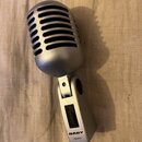 Stříbrný mikrofon s retro designem a mřížkou v horní části. Na spodní části těla je vypínač s nápisem OFF a značka NADY s doplňujícím textem Dynamic.…