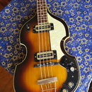 Elektrická basová kytara s polodupatým korpusem v barevném přechodu od žluté k tmavě hnědé. Nástroj má bílý perleťový pickguard a dva snímače s kovov…
