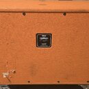Kytarový reproduktorový box v oranžovém texturovaném potahu. Uprostřed zadní strany je černý štítek s nápisy: "orange", "FPC212-V30C-4x8", "MADE IN E…