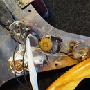 Fotografie zachycuje vnitřní elektroinstalaci elektrické kytary s kovovou stíněcí vrstvou v korpusu. Jsou vidět tři potenciometry, zapojení kabelů a…